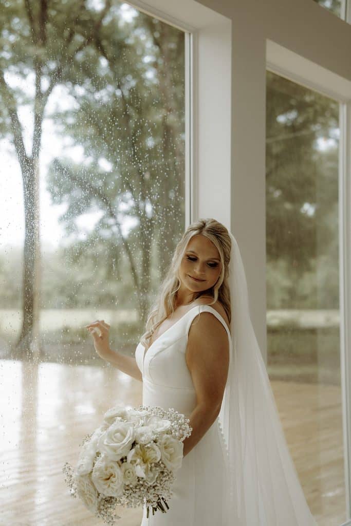 bride standing in front of the window, looking back while wearing her wedding gown, white flower bouquet, Orlando, FL