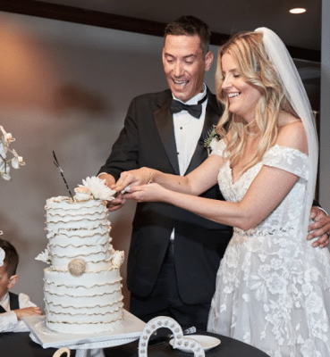 bride and groom cutting their wedding cake, large two tier cake with white frosting with ruffles and gold embellishments, Orlando, FL
