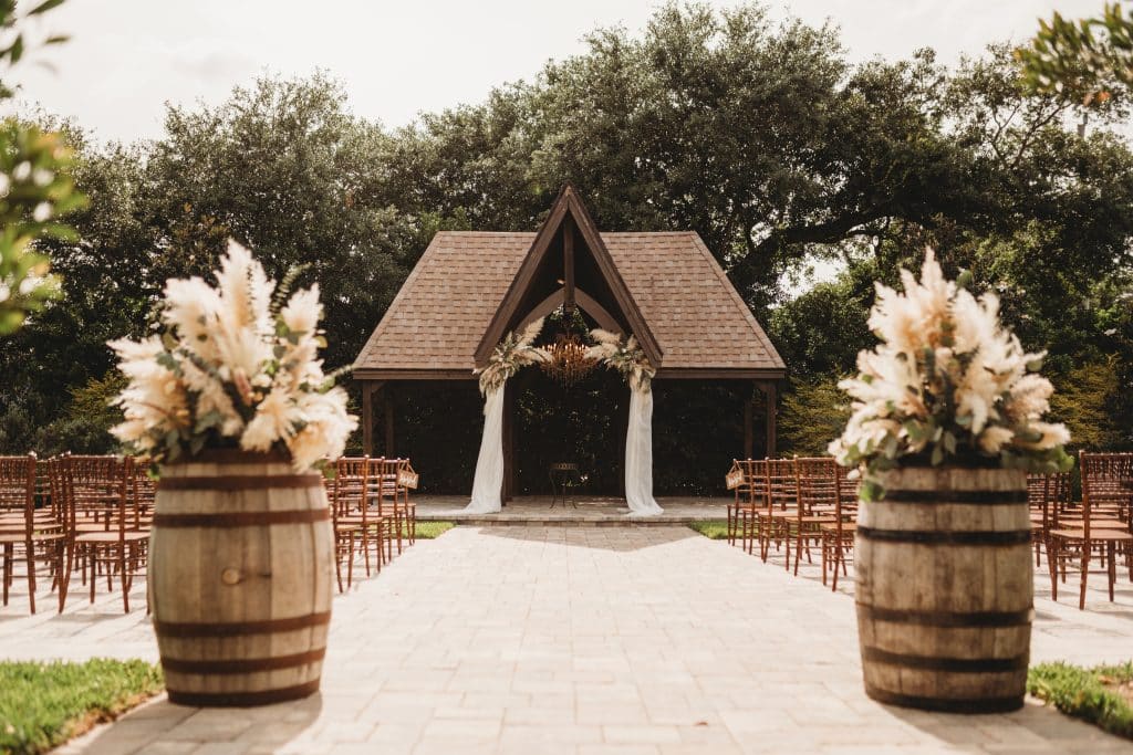 Wedding Ceremony set up, whiskey barrels with large floral arrangements, small pavilion with the altar in front, The Enchanting Barn, Orlando, FL