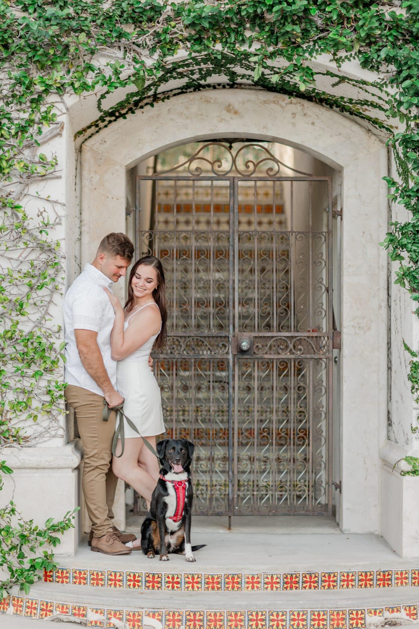couple posing for picture with dog in front of wrought iron gate doorway