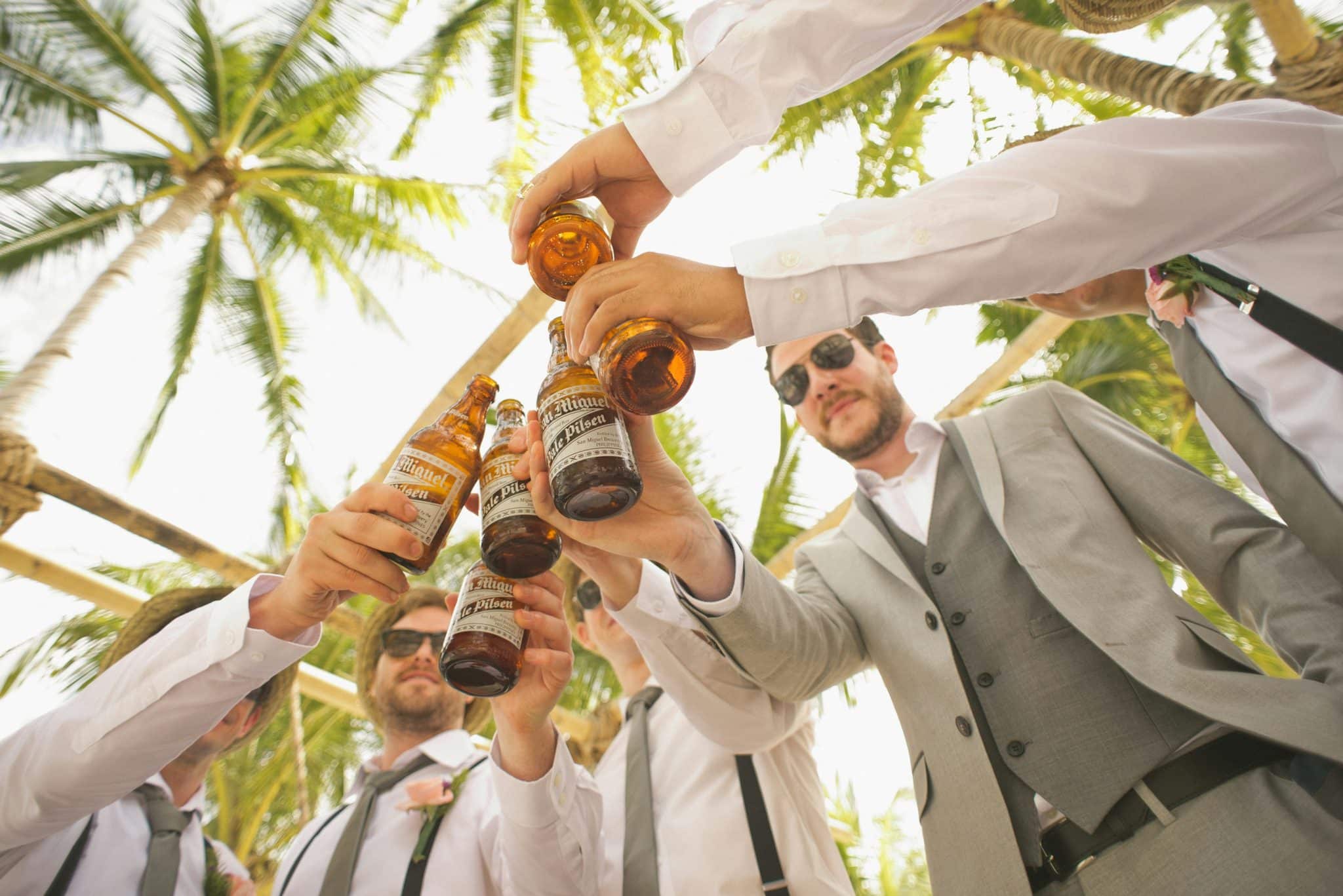 group of guys toasting beers outside under palm trees on European bachelor party