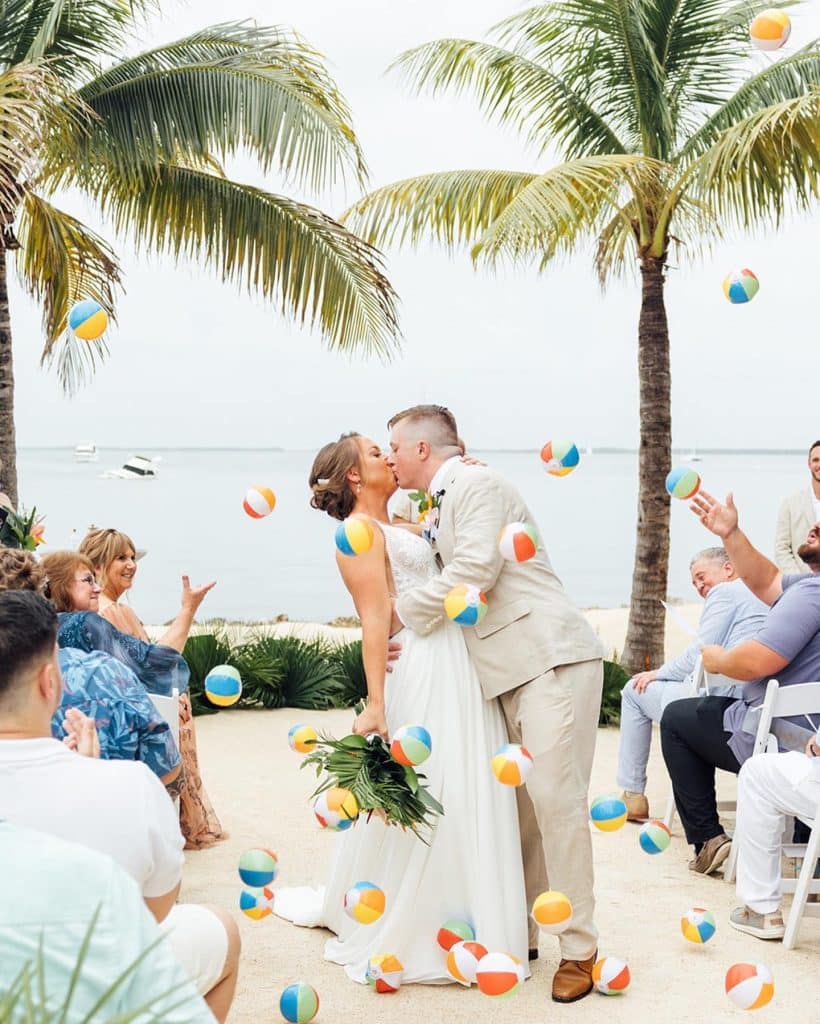 married couple kissing after their wedding ceremony, outdoors, beach, palm trees, beach balls, water, Orlando, FL