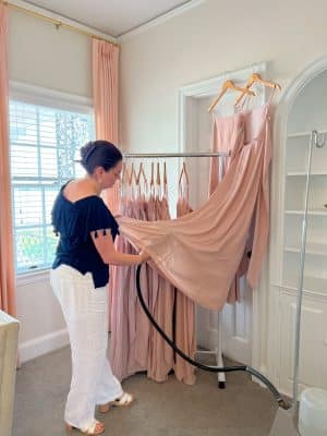 woman looking at the hem of a link dress hanging from a door frame, rack with multiple pink dresses, Orlando, FL