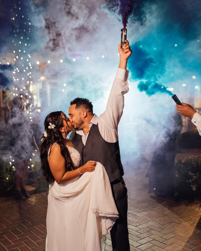 bride and groom kissing while setting off a color bomb of blue at their reception, Orlando, FL