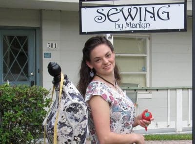Marilyn standing outside her office with a mannequin, measuring tape, Sewing by Marilyn sign, Orlando, FL
