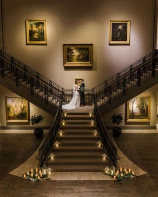 bride and groom standing on the landing of the grand staircase with candles lit at the bottom, Author Made Photo and Video, Orlando, FL