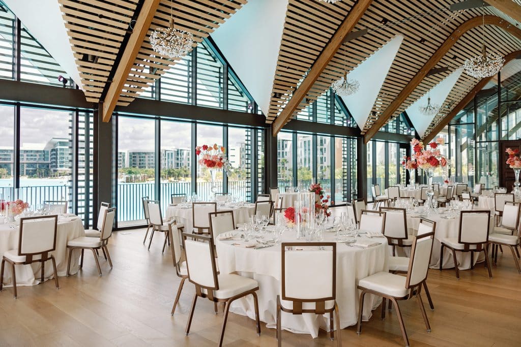 indoor reception set up, white tablecloths, white chairs with brown outlines, large windows with blinds facing the water, Orlando, FL
