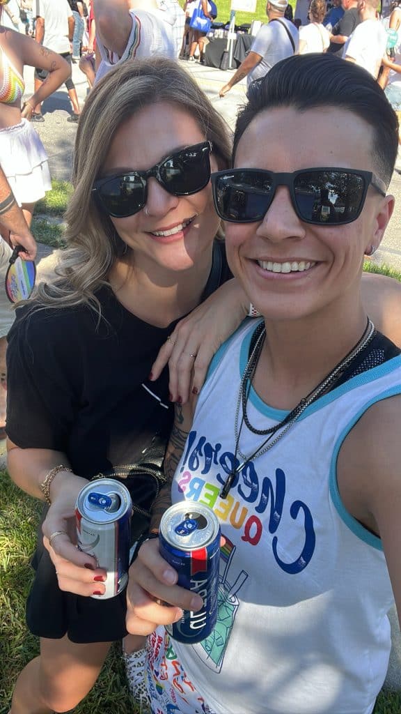 couple stand together with beers in hand and sunglasses on for picture