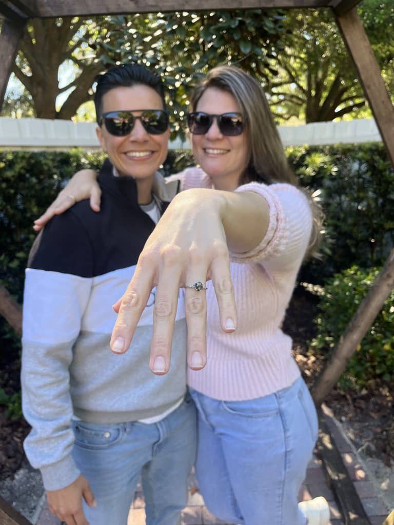 couple stand together posing for picture with sunglasses on holding hand out after historic venue 1902 marriage proposal