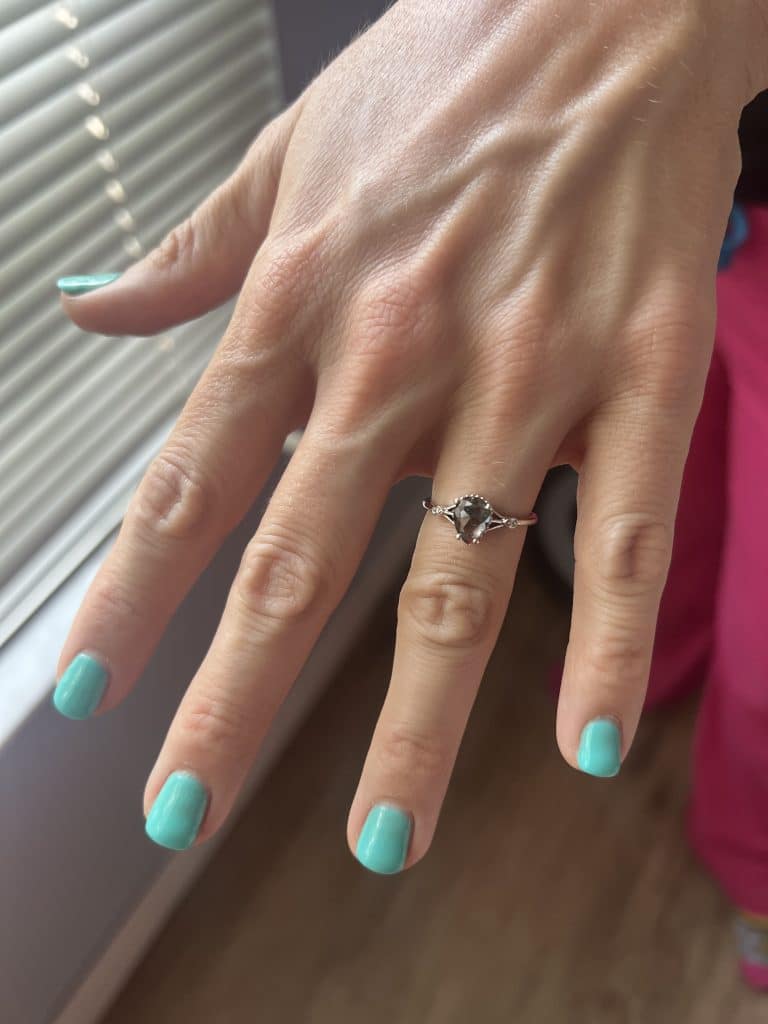hand with teal fingernails and engagement ring on hand