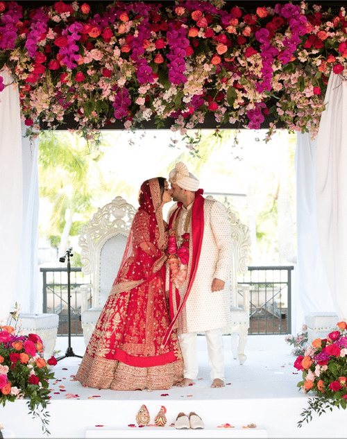 bride and groom kissing after their ceremony, pink and red flowers, traditional Indian wedding attire, outdoors, Naomi Zora Events, Orlando, FL