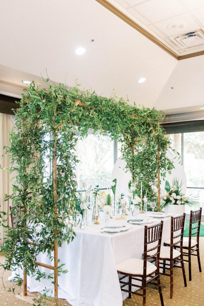 reception table set for 6, white tablecloth, black chairs, greenery hung above on a structure above the table, Orlando, FL