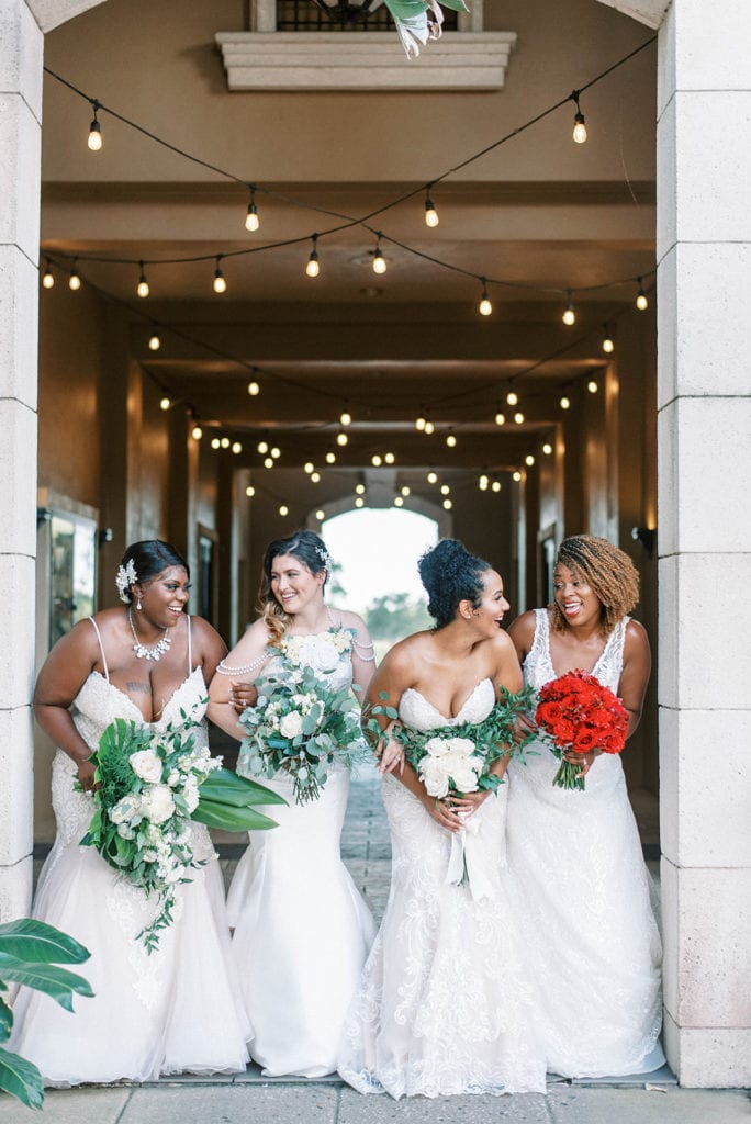 four brides posing together with their floral bouquets, twinkle lights above, entry way into the reception hall, Orlando, FL