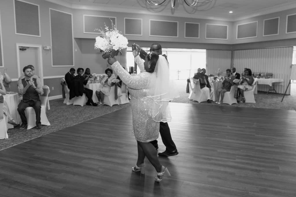 black and white photo of the bride and groom arriving at their reception, bride holding her bouquet in the air, wood dance floor, guests watching on, Ventura Country Club, Orlando, FL