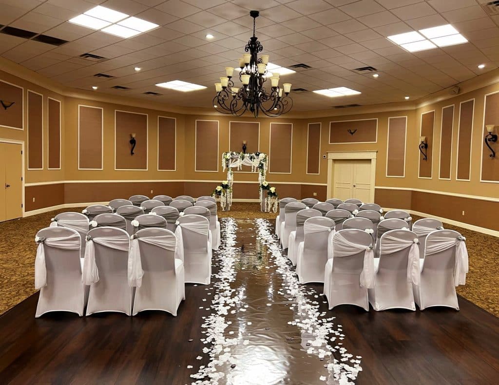 ceremony set up, indoors, white flowers lining the aisle, white chairs with white backs, small floral arrangement at the front of the aisle at the altar, Orlando, FL