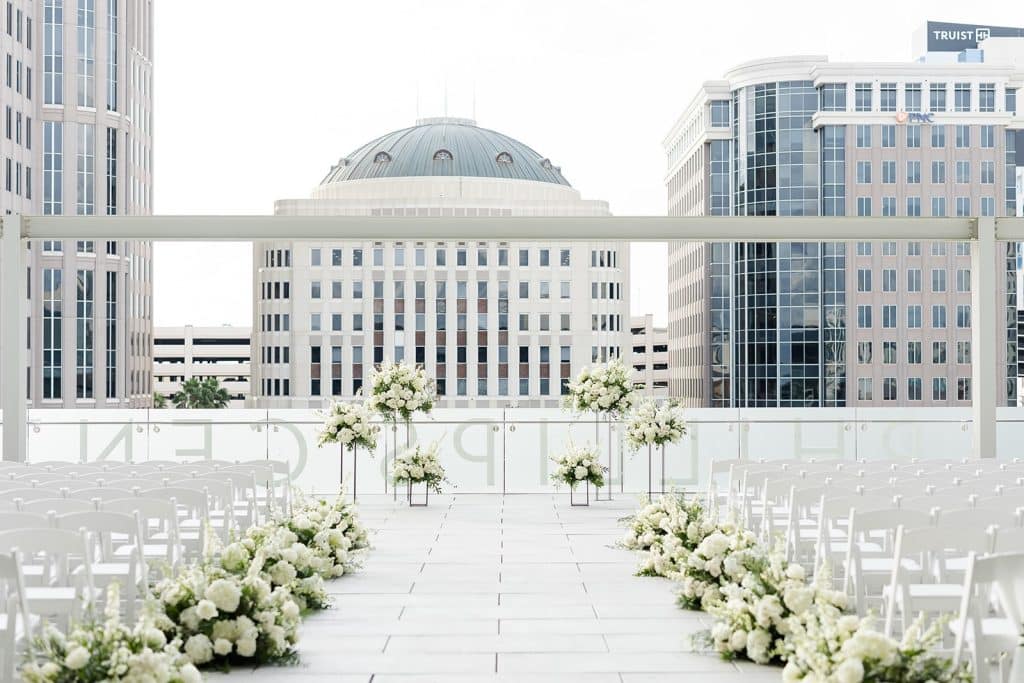 roof top wedding ceremony set up, white chairs in rows with a center aisle, floral arrangements on each row and at the front near the altar area, Orlando, FL