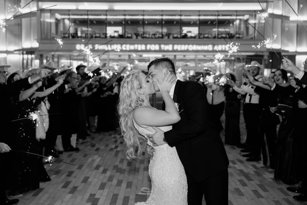 black and white photo of bride and groom kissing with their wedding guests cheering them on, Dr. Phillips Center for Performing Arts, Orlando, FL