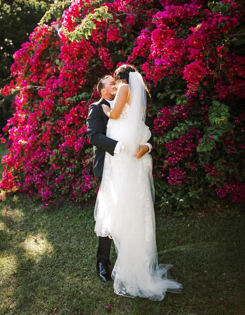 bride and groom embracing near a pink flowered bush, Melanie Paige Events + Design, Orlando, FL