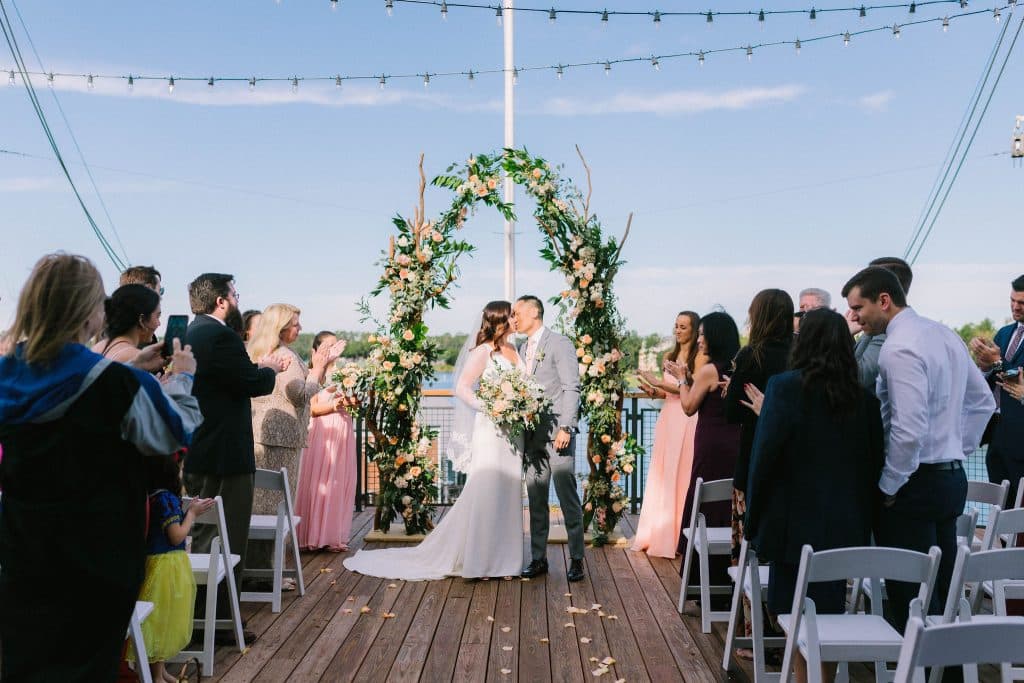 wedding ceremony on the deck, floral arch, guests cheering on the couple as they kiss, Paddlefish, Orlando, FL