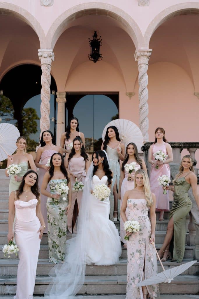 bride and her wedding attendants standing on the venue stairs, outdoors, wearing pink or green dresses, Melanie Paige Events + Design, Orlando, FL