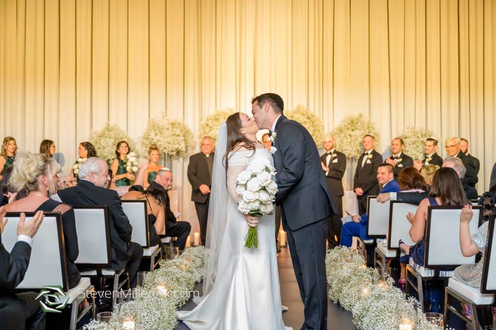 bride and groom kissing in the center of the aisle, guests in their seats watching as the wedding party stands at the front of the room, Orlando, FL