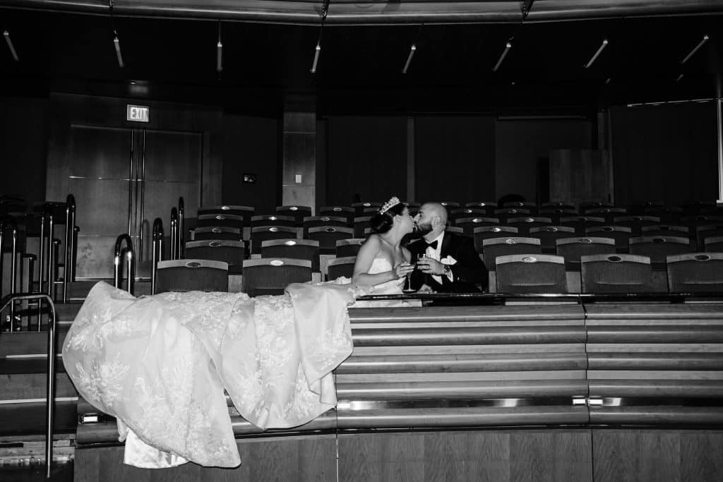 black and white photo, bride and groom kissing in an auditorium, seated, wedding dress train draped over the seats, Orlando, FL