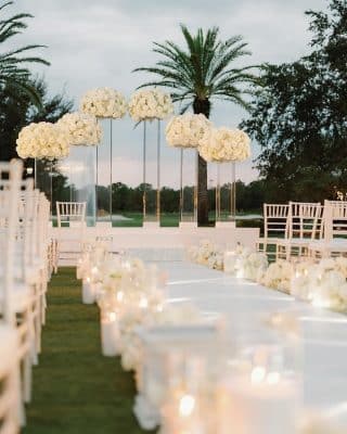 wedding ceremony, outdoors, candles lit at the end of each aisle, large white floral arrangements on pillars, at different heights at the front, palm trees, Orlando, FL