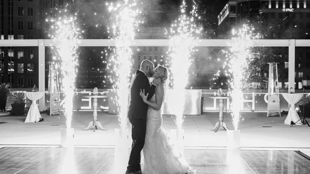 black and white photo, bride and groom kissing on the dance floor, outdoors, rooftop, fireworks going off in a set of four, Orlando, FL