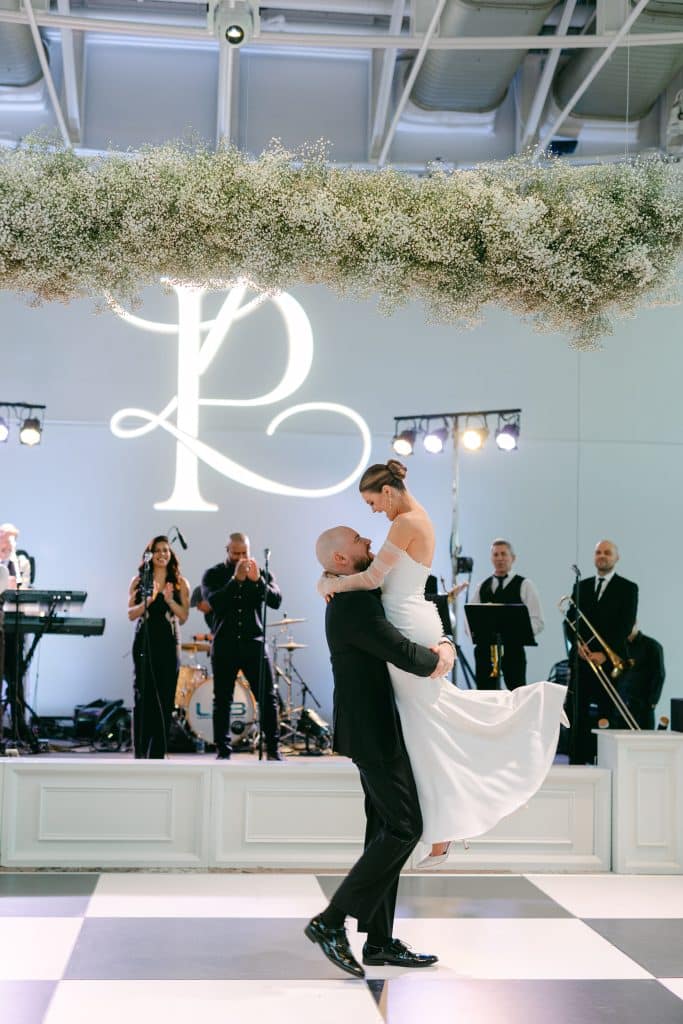 groom lifting his bride on the dance floor, band playing on the stage, neon lights of R & L intertwined, Orlando, FL