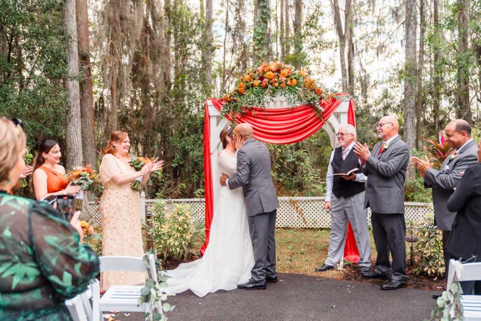 bride and groom with the wedding attendants, outdoors, sunflowers atop the altar, red and white fabric adorning it, Orlando, FL