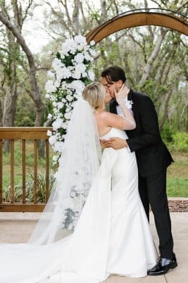 bride and groom kissing under the arch, adorned by white flowers on the left, Orlando, FL