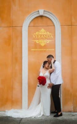 bride and groom, red rose bouquet, archway with a glass display of the Veranda Elegant Events logo on it, Orlando, FL
