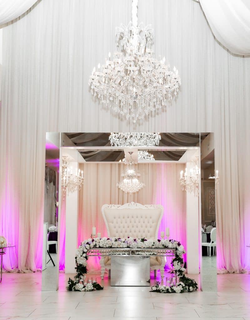 head table at the reception, purple uplighting, large white love seat, chandelier, floral garland on the head table, Veranda Elegant Events, Orlando, FL