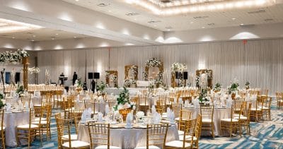 closer view of the ballroom, set for a wedding reception, gold chairs with white seats, green and white floral garlands throughout the room, Orlando, FL