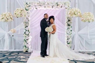 bride and groom in their wedding gown and suit, standing in front of a photo station, white floral garland, white and light purple sheer fabric, Orlando, FL
