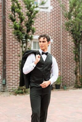 groom posing in his tuxedo, outdoors, in front of the venue, brick wall, jacket over the shoulder, Orlando, FL