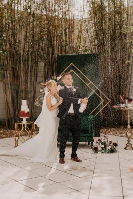 bride and groom in their wedding attire, wedding cake on a small table, metal pergola in a tilted square shape, tall branch trees, Orlando, FL