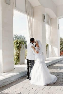 bride and groom embracing, outdoors, white walls with openings of sheer white curtains, Orlando, FL