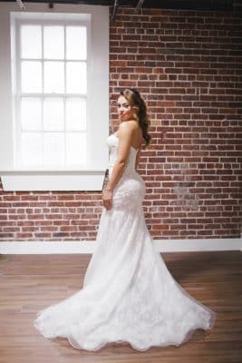 bride in her wedding dress, looking back at the camera, open room, brick wall, white window frame, Orlando, FL