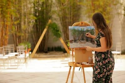 woman standing in a space set for a wedding ceremony, painting on a canvas adhered to an easel, Renaissance Orlando Resort and Spa, Orlando, FL