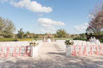 wedding ceremony set up outdoors, peach material tied to the back row of chairs, pergola wrapped in the same peach material, brick patio, Orlando, FL