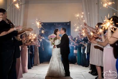 Bride and groom share a kiss during a sparkler exit sendoff at Renaissance Orlando Resort near Disney Springs, surrounded by guests holding lit sparklers in a romantic evening ceremony departure