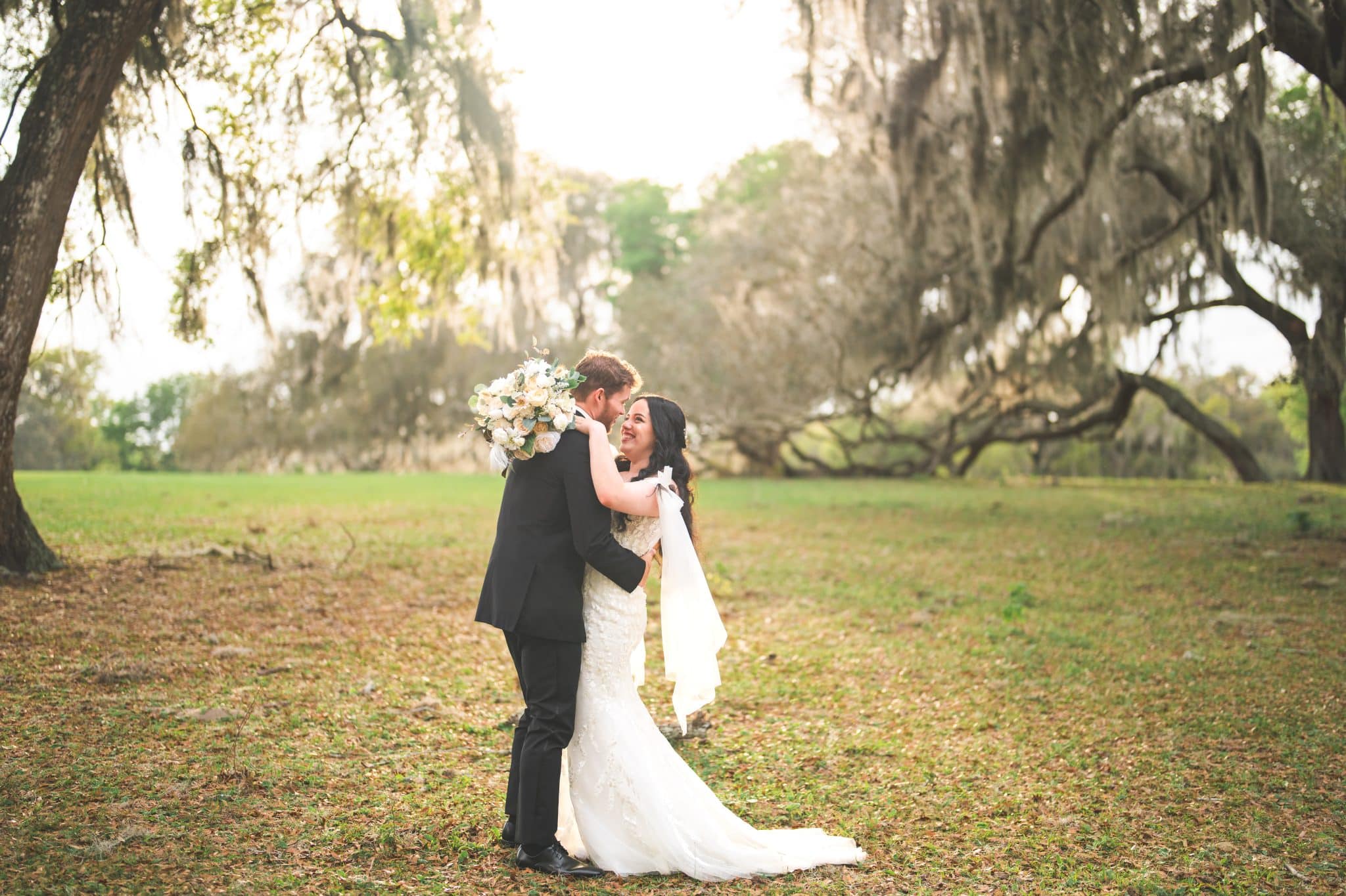 bride and groom embracing towards a kiss with a gorgeous forest background with the bright sun shinning through 