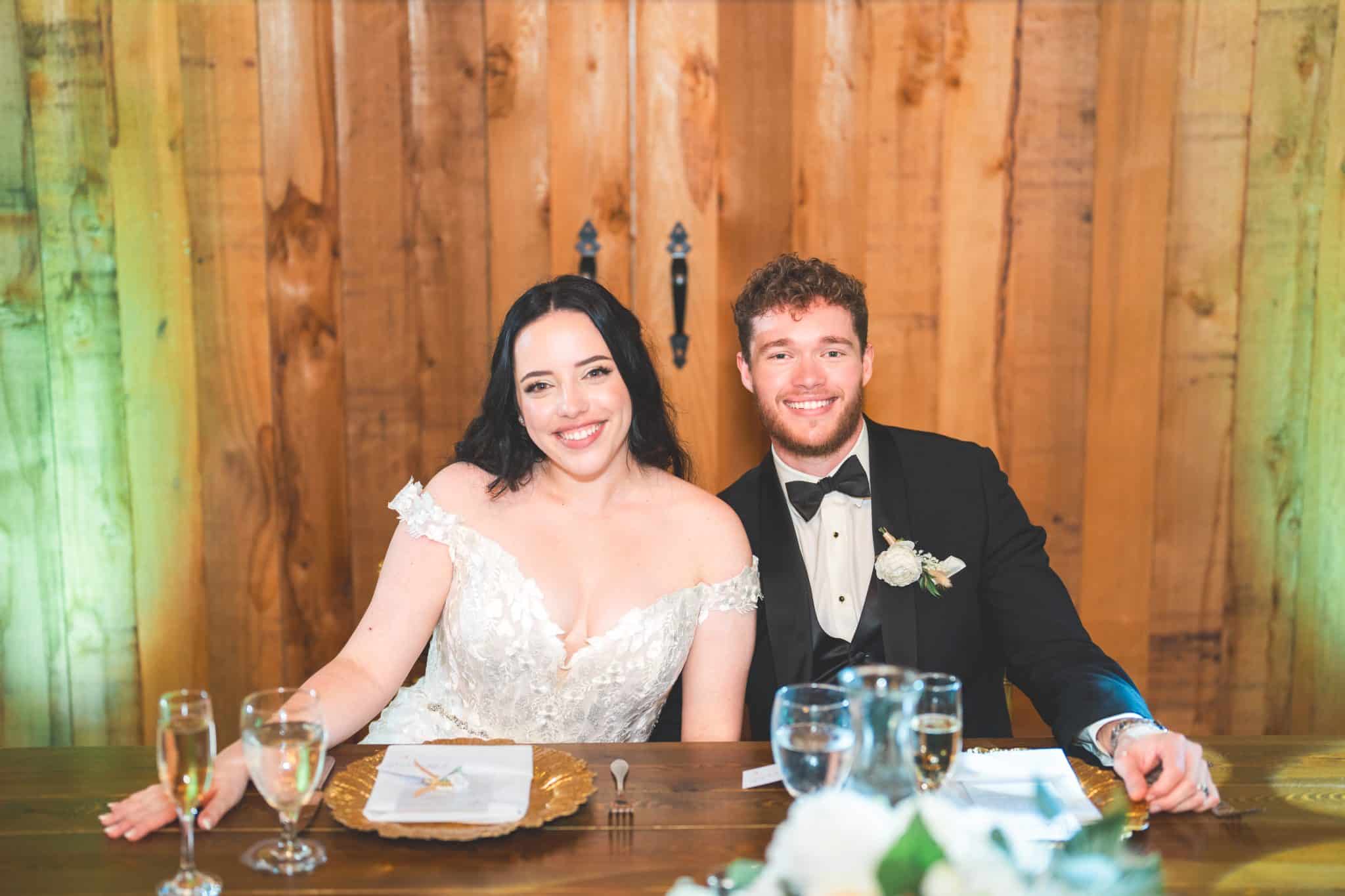 bride and groom at the couples table smiling with a wooden door background and gold chargers on table