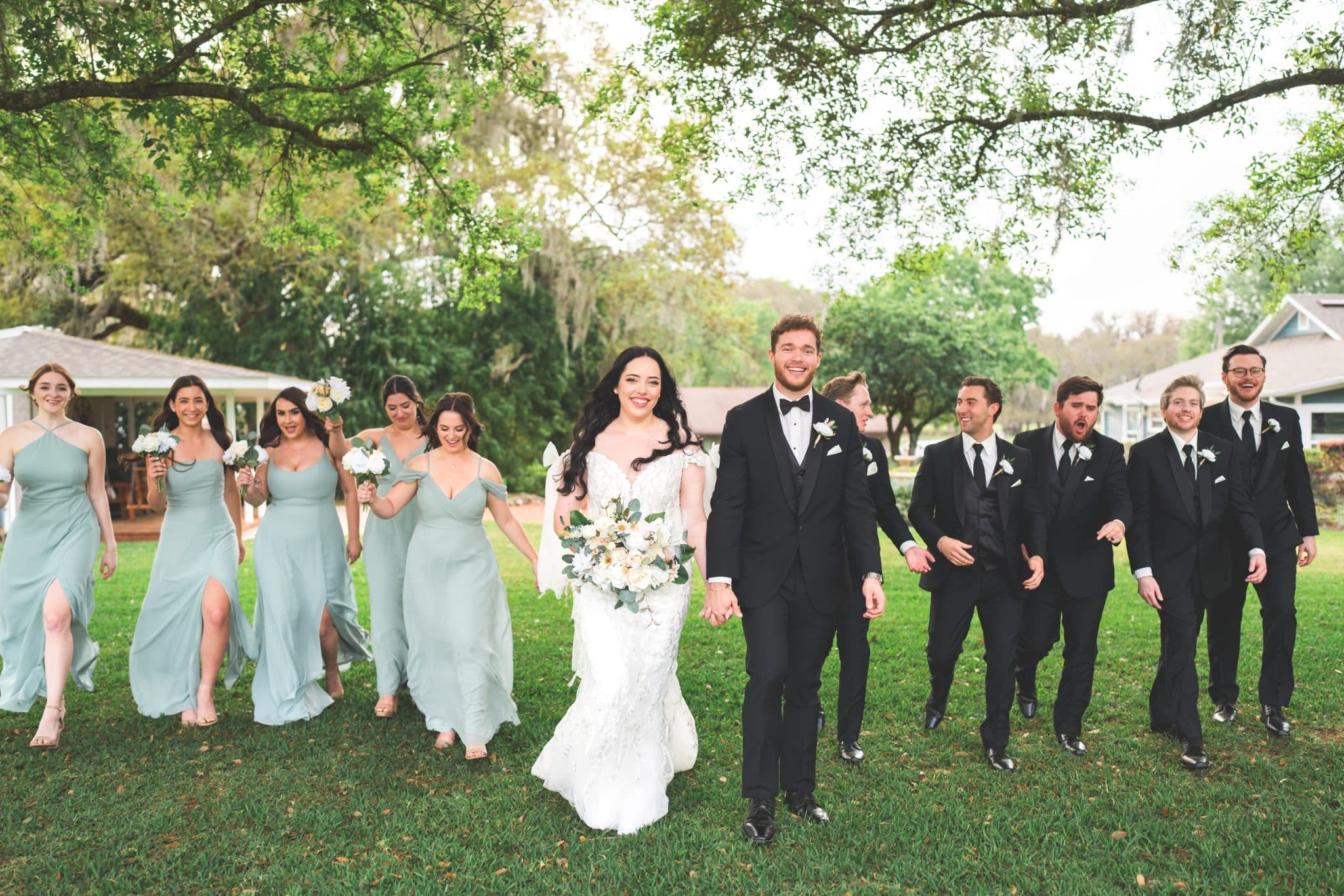 couple along with bridal party walking in a forest farmhouse venue Moss Estates posing for wedding pictures