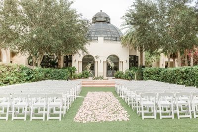 rows of chairs set with a center aisle for a wedding ceremony, pink rose petals set in the aisle, altar at the front, The Alfond Inn behind the lawn, Orlando, FL
