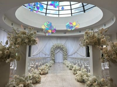 indoor atrium area, colorful decor hanging from the ceiling, set for a wedding ceremony, rows of white chairs with a center aisle, white floral bunches everywhere, Orlando, FL