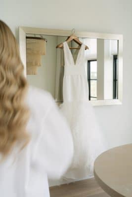 bride in her white wedding robe, wedding dress hanging on the mirror, Orlando, FL