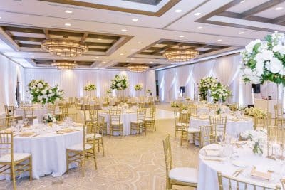 ballroom set up for a reception, round tables, white tablecloths, gold chairs with white cushions, large white floral centerpieces, Orlando, FL