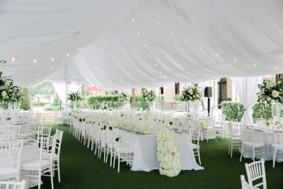 outdoor white tent filled with long rectangular tables, white floral centerpieces down the center of each table, white chairs, white tablecloths, string lights displayed across the tent, The Alfond Inn, Orlando, FL